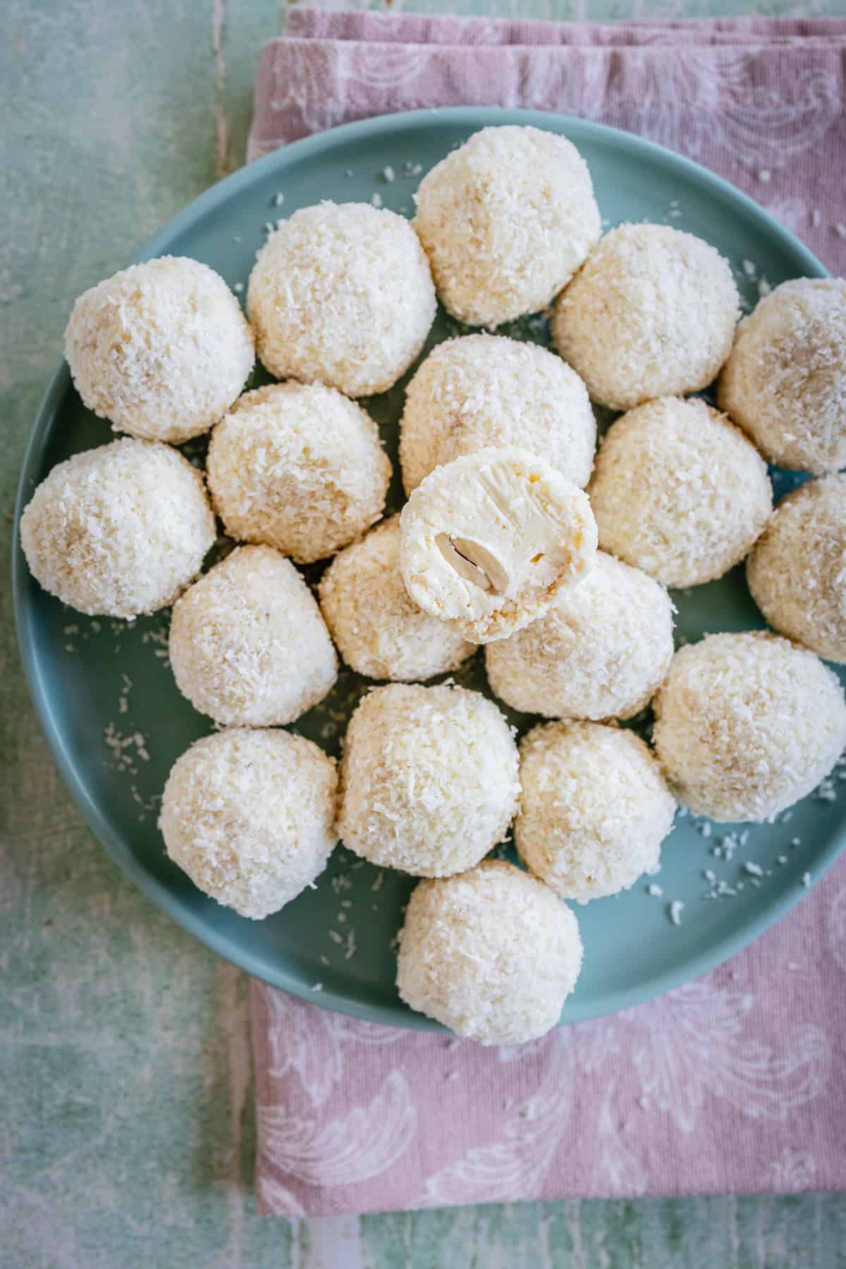 White coconut balls on a plate one cut in half with almond inside