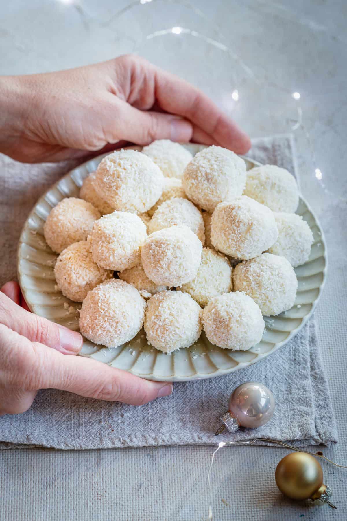 two hands holding a plate of white coconut balls