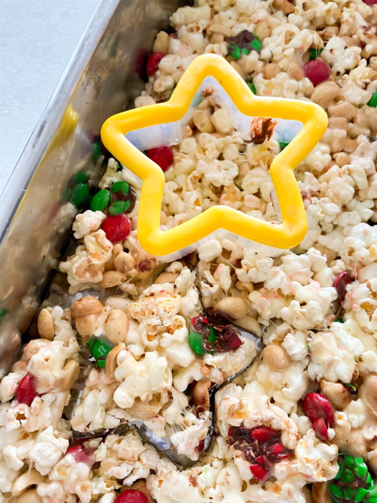 using a star cookie cutter to cut the shape into a sheet of marshmallow popcorn treats.