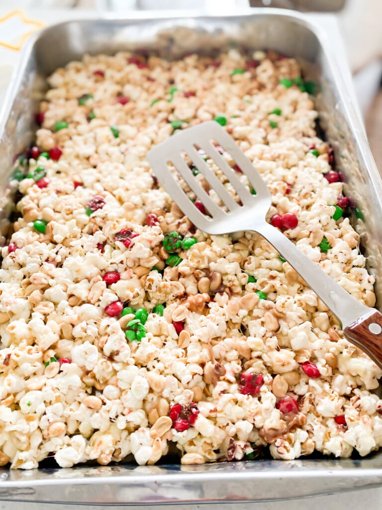 pressing mixed popcorn, marshmallows, peanuts and butter into a baking tray.