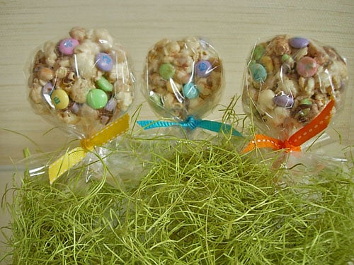 Popcorn-Cake-Lollipop recipe and directions Popcorn-Cake recipe made into lollipop shapes with sticks poked into them. Ribbon tied around sticks and placed on Easter grass.