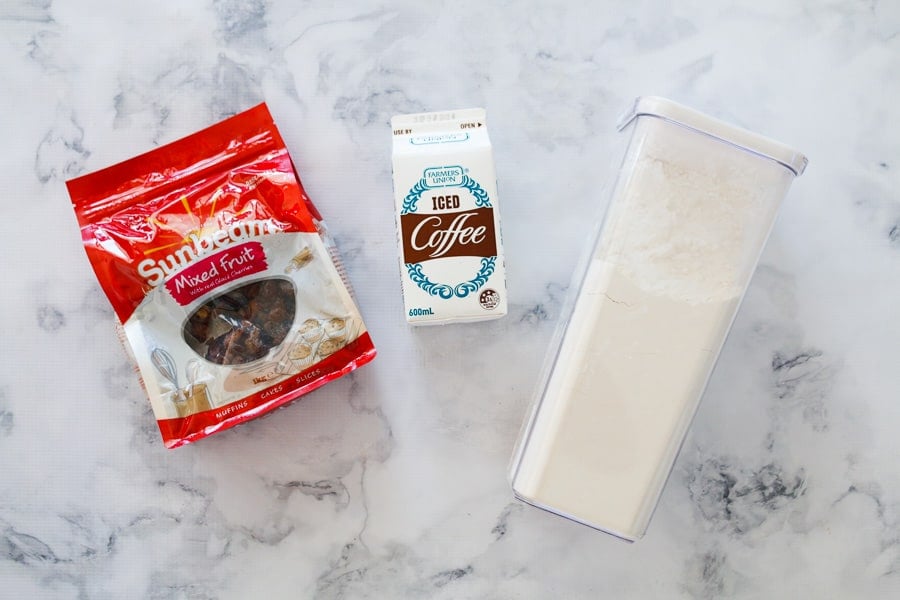 Mixed dried fruit, iced coffee and self-raising flour on a bench - the 3 ingredients for a fruit cake.