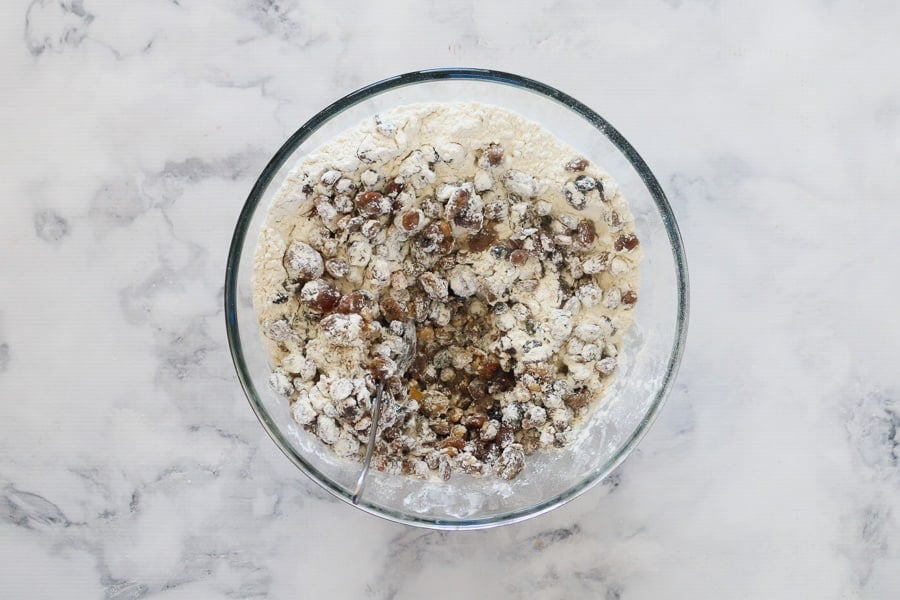 An overhead shot of a bowl with self-raising flour being added to soaked dried fruit.