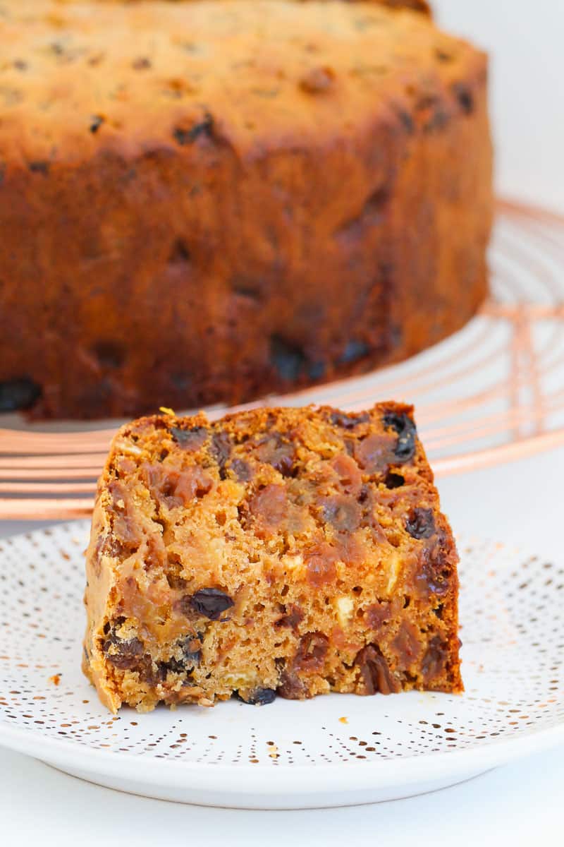 A piece of fruit cake with the whole cake in the background.