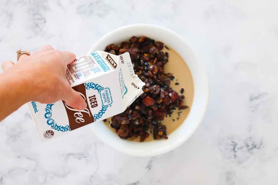 Iced coffee being poured into a bowl of dried mixed fruit.