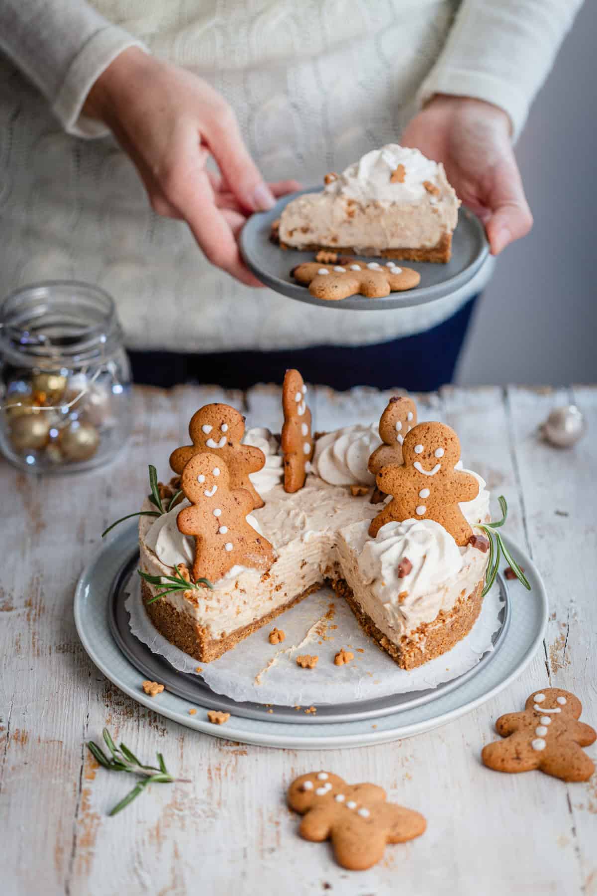 a woman holding a slice of cheesecake over the sliced whole decorated with cookies