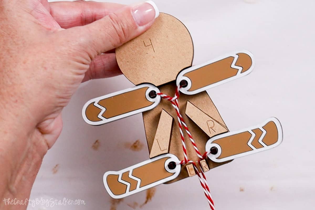 Testing the movement of the gingerbread man ornament's pull-string mechanism, showcasing the interactive motion of its arms and legs tied with red and white twine.