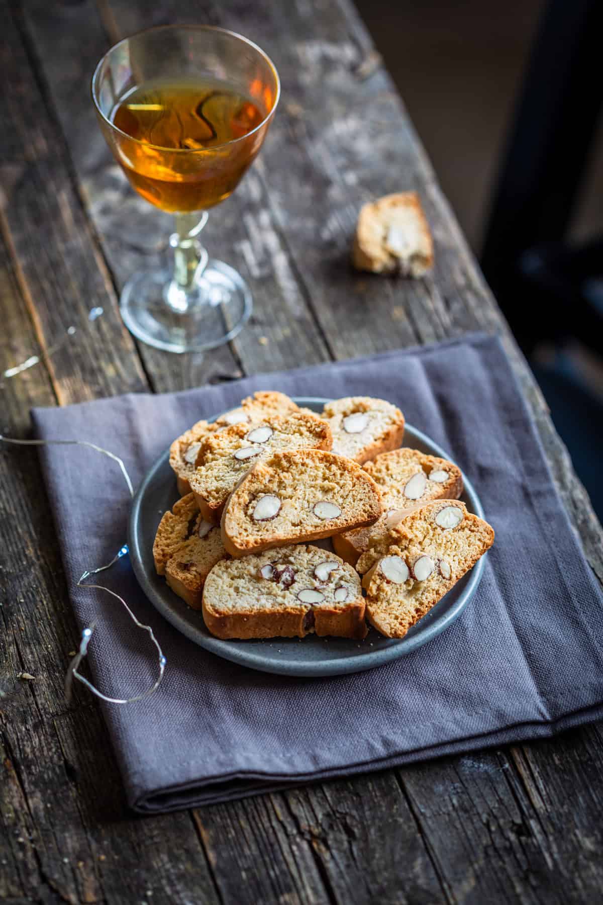 a plate with cantucci next to Vin Santo on a wooden table