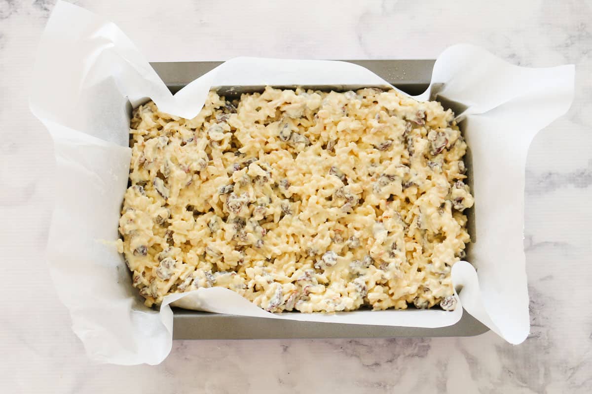 White Christmas slice being pressed into a baking tin lined with baking paper.