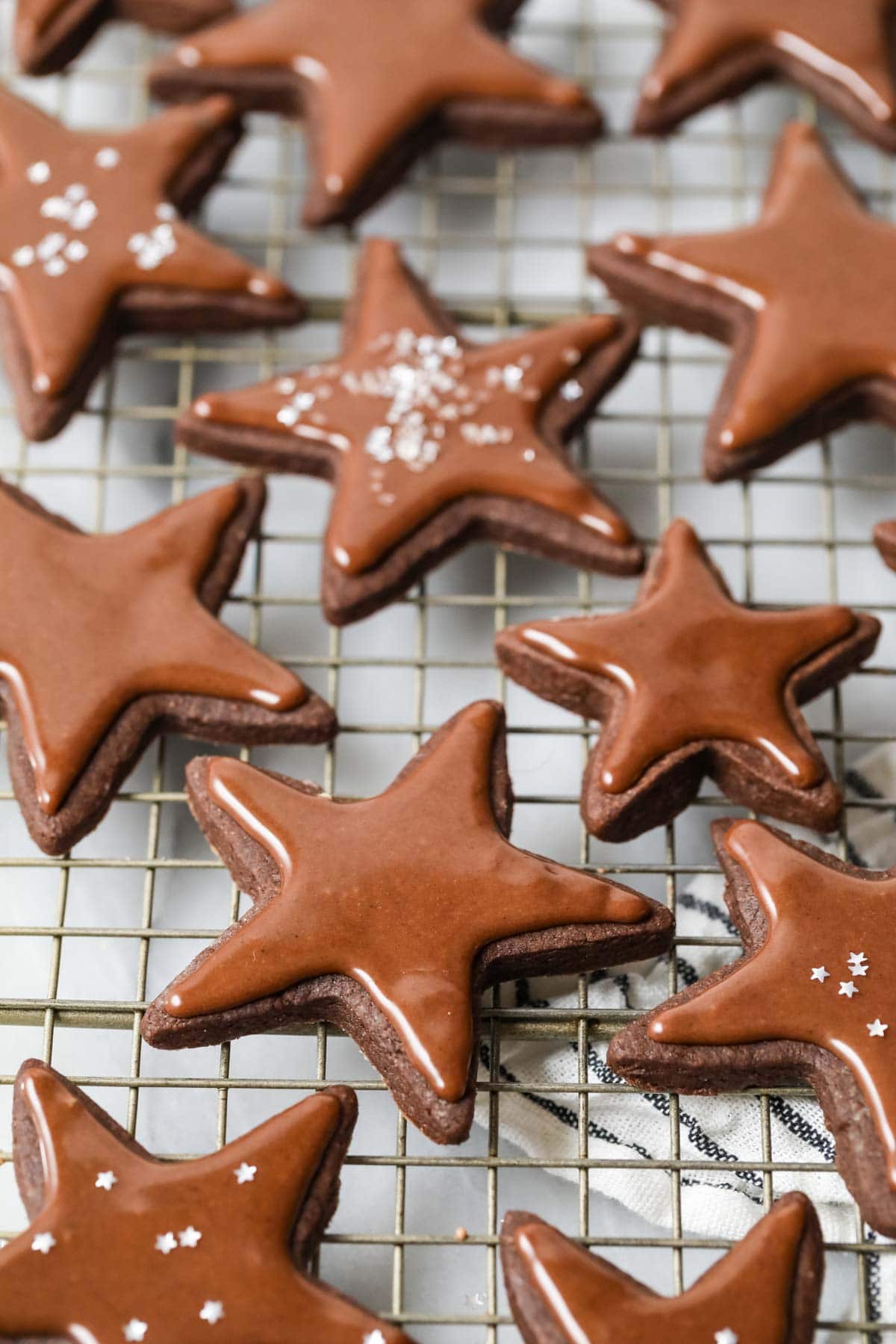 Cooling rack of chocolate sugar cookies topped with shiny chocolate icing.