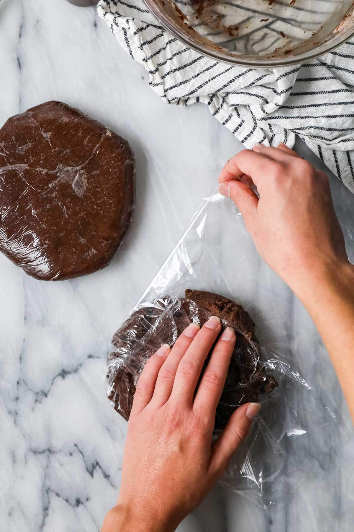 Hands wrapping a disc of chocolate dough in plastic wrap before chilling.