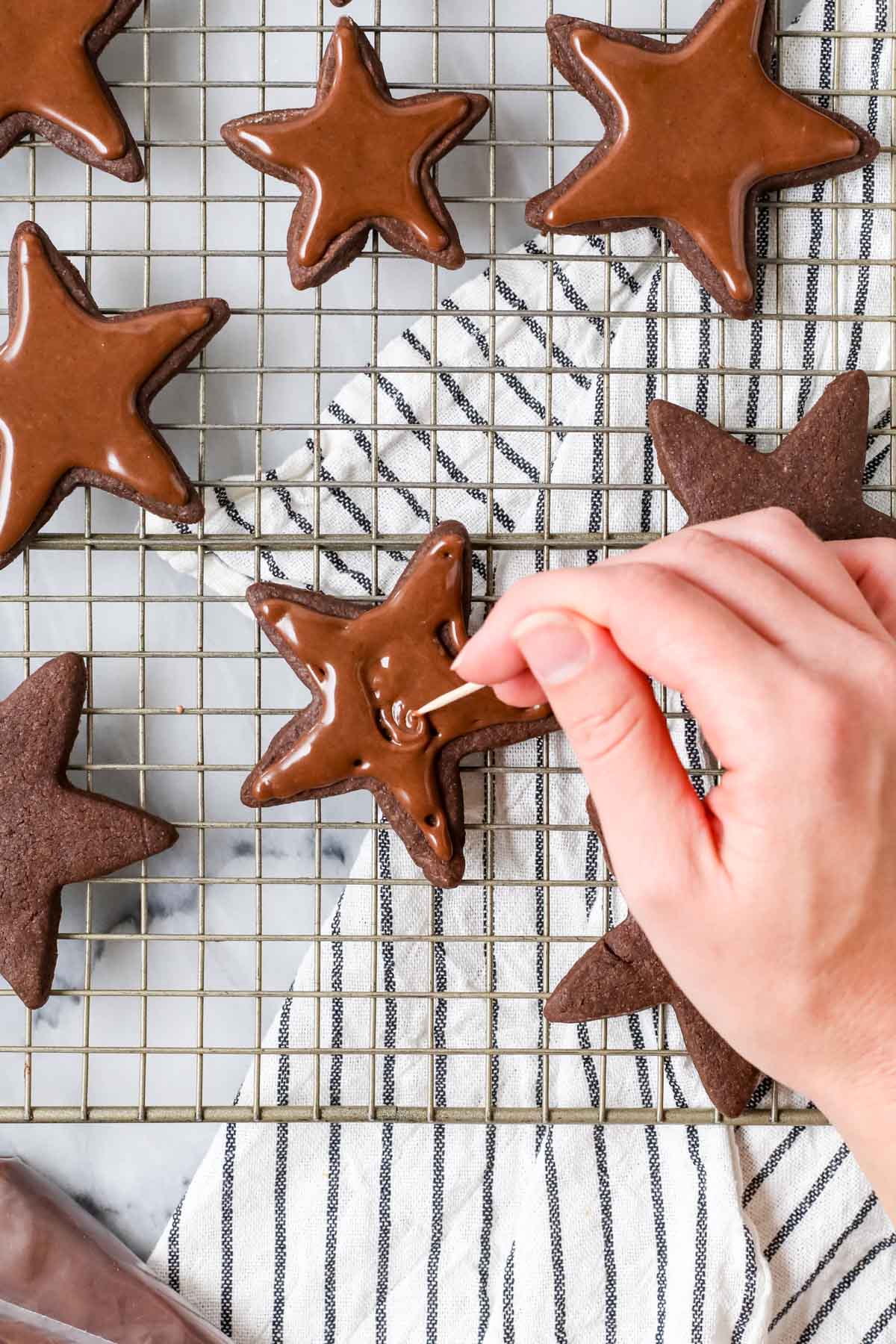 Using a scribe tool to smooth chocolate frosting onto chocolate star sugar cookies.