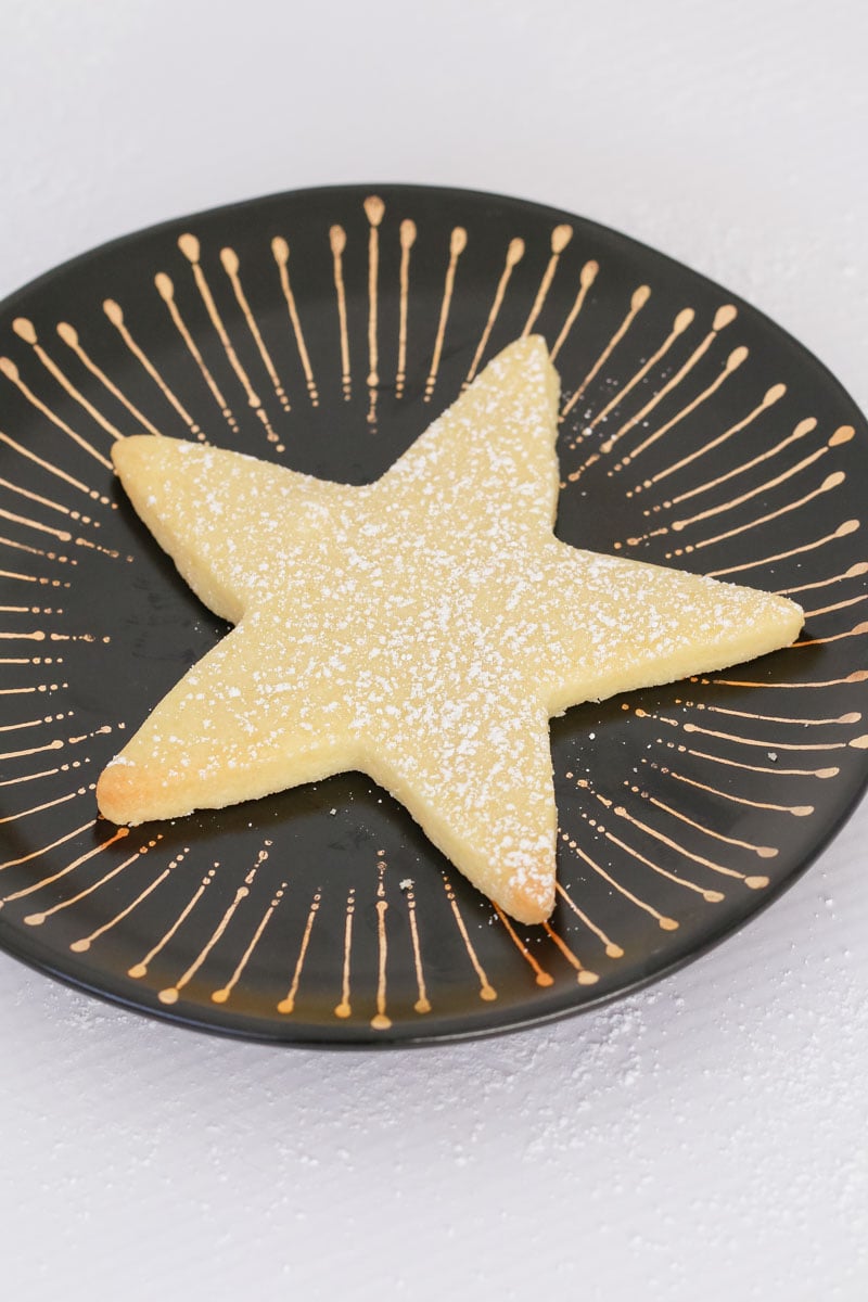 A shortbread star on a black and gold plate sprinkled with icing sugar. 