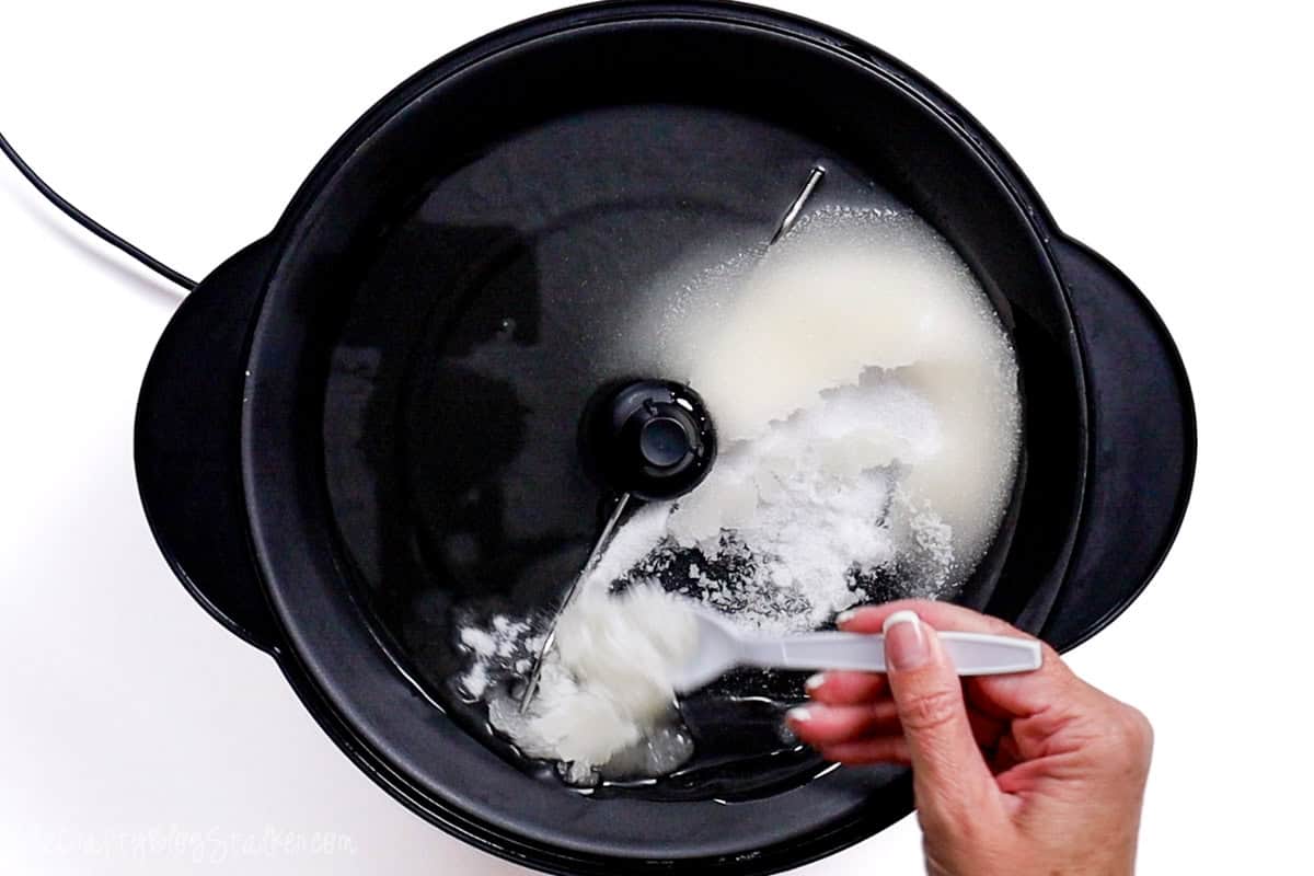 A hand stirring sugar and oil in a Stir Crazy popcorn maker, preparing the base for homemade kettle corn.