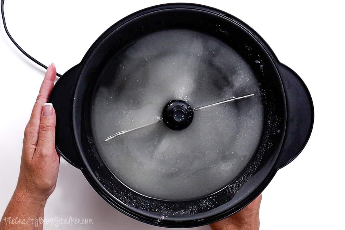 A Stir Crazy popcorn maker with sugar and oil inside, ready to start making sweet and salty kettle corn, as hands hold the sides of the machine.