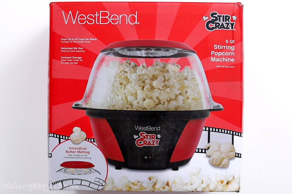 The red packaging of the WestBend Stir Crazy 6-Qt Stirring Popcorn Machine, featuring a clear bowl filled with fluffy popped popcorn, highlighting its butter-melting feature.