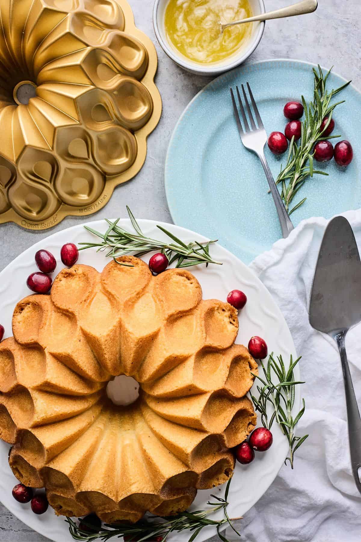 An eggnog cake on a white platter garnished with cranberries and sprigs of rosemary.