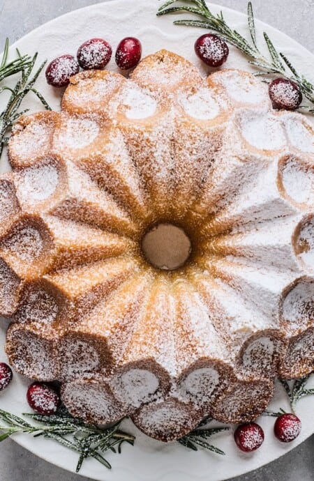 A buttered rum eggnog cake on a plate garnished with cranberries and rosemary.