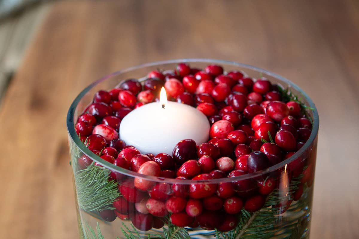 A floating candle on top of fresh cranberries in a clear vase jar