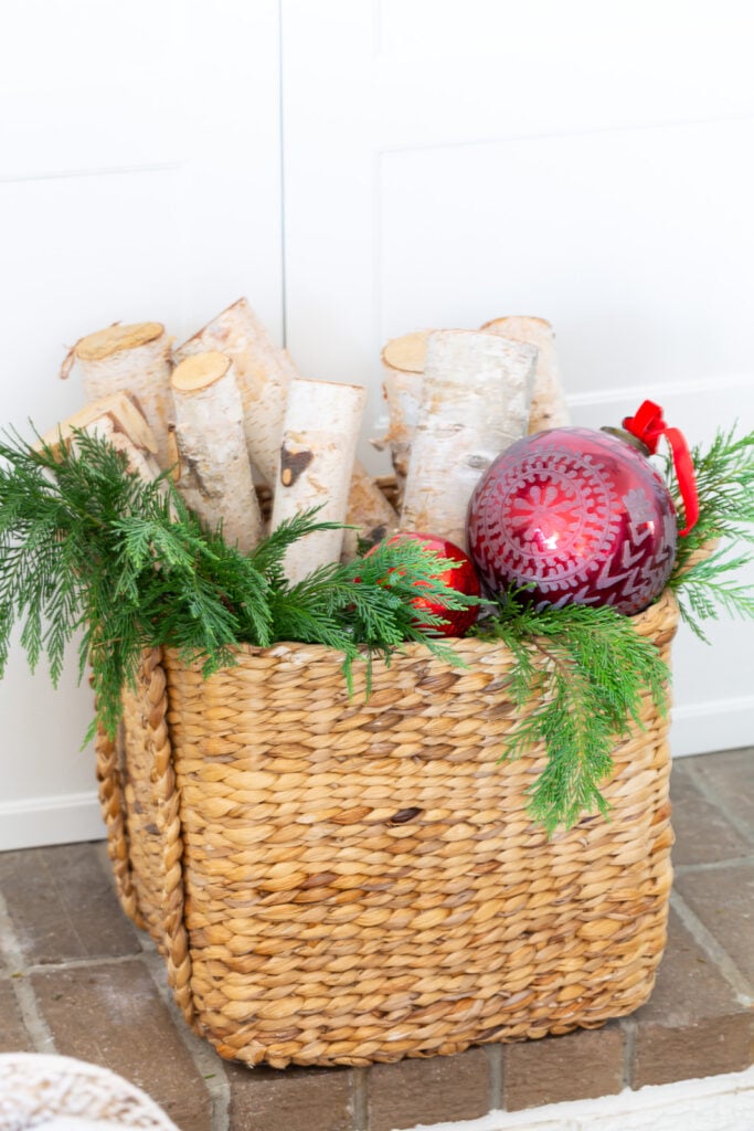 Basket filled with firewood, greenery and red Christmas ornaments.