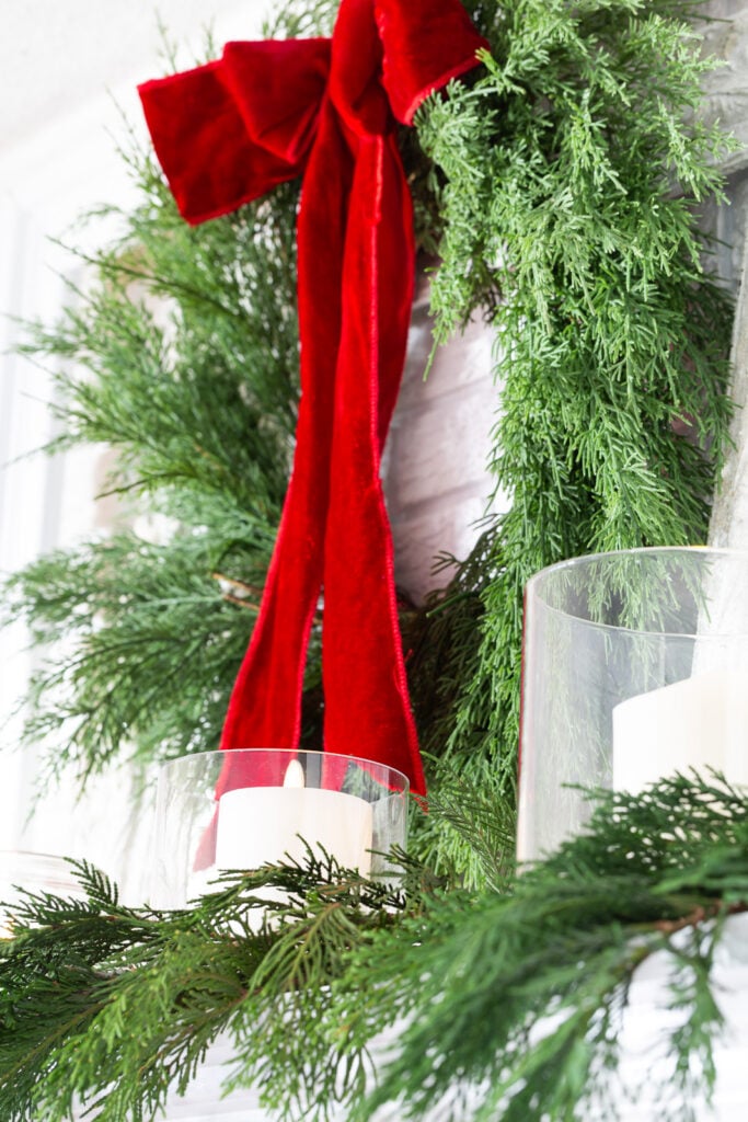 Wreath with red velvet ribbon hanging on a wall above a fireplace mantel.
