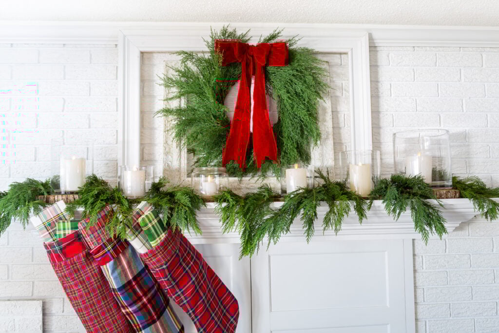 White fireplace mantel decorated for Christmas in a red, green and plaid color scheme.