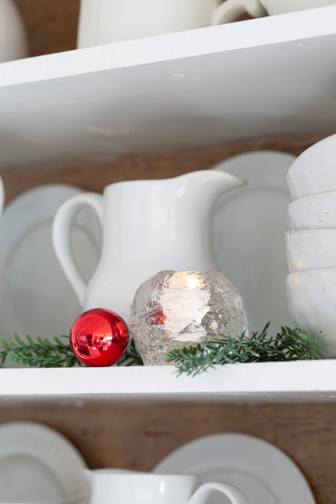 White pitcher with greenery and red Christmas ornament open shelves in kitchen.