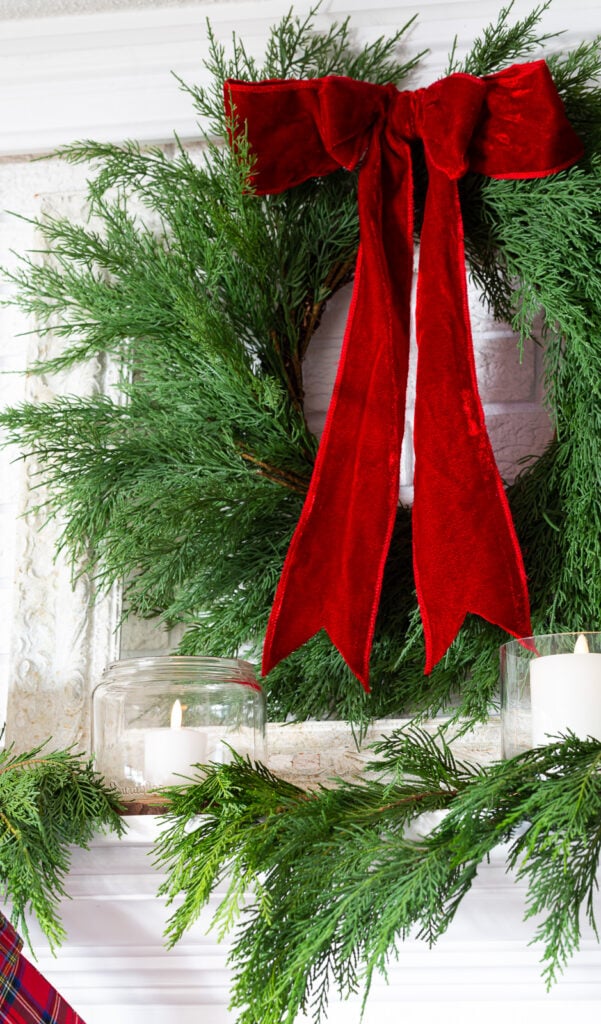 Wreath with red velvet ribbon hanging on a wall above a fireplace mantel.