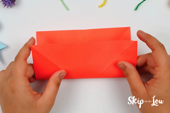 Two hands turning the paper 90 degress and making the same fold from the bottom towards the top to form a rectangle.