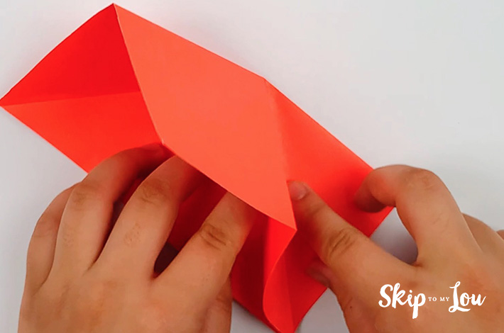Two hands folding the paper inwards along the crease line.