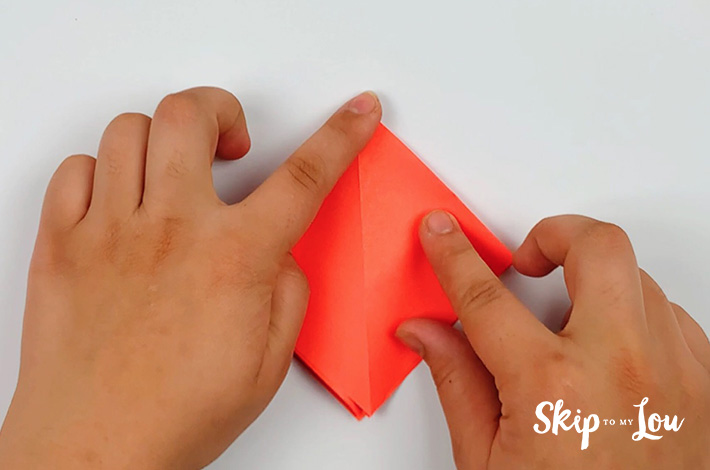 Two hands finishing the fold to form a kite shape.