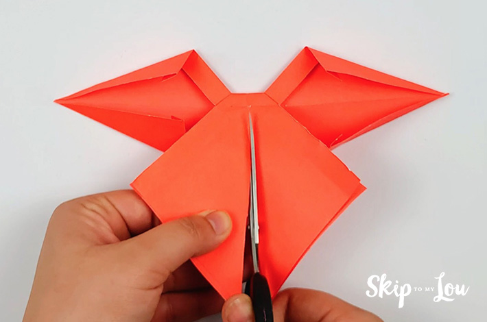 Two hands holding a scissors and cutting from the bottom of the bottom piece of paper upwards.