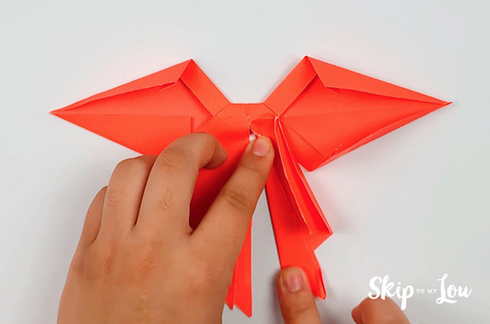 Two hands folding the right hand bow tail.
