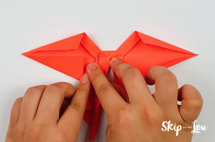 Two hands folding the left hand bow tail.