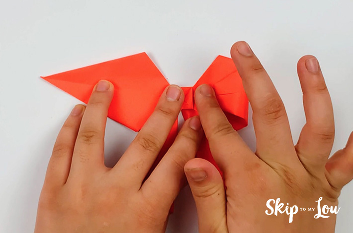 Two hands folding the left and right point into the center of the bow.