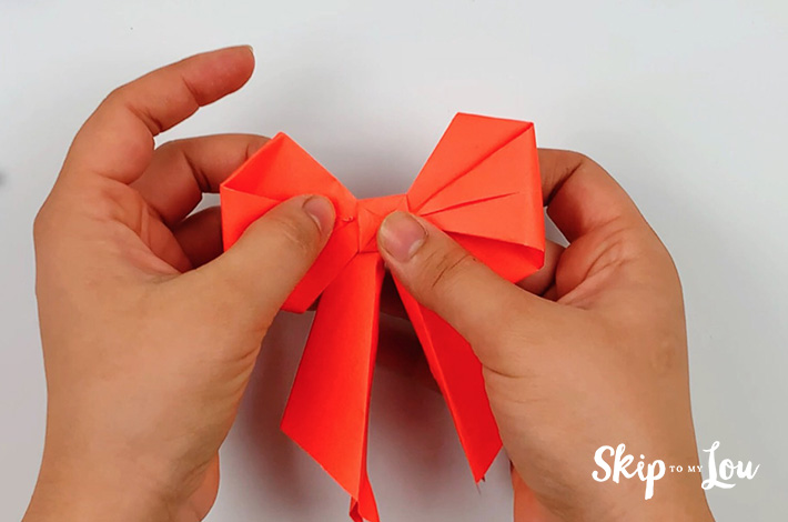 Two hands folding the left and right point into the center of the bow.