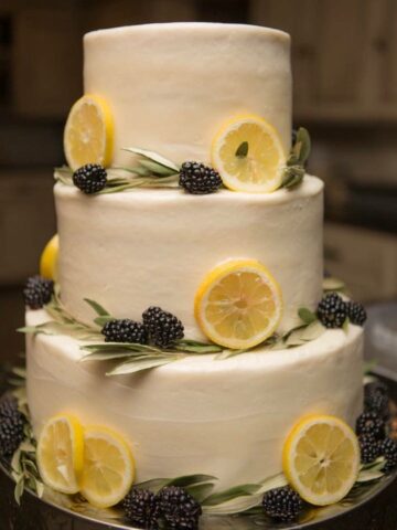 summer themed wedding cake with lemon curd cake, decorated with white vanilla buttercream, rosemary, lemon slices, and fresh blackberries.