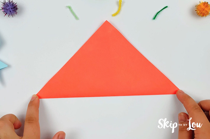 Two hands folding the square piece of paper at a 45-degree angle to form a triangle.