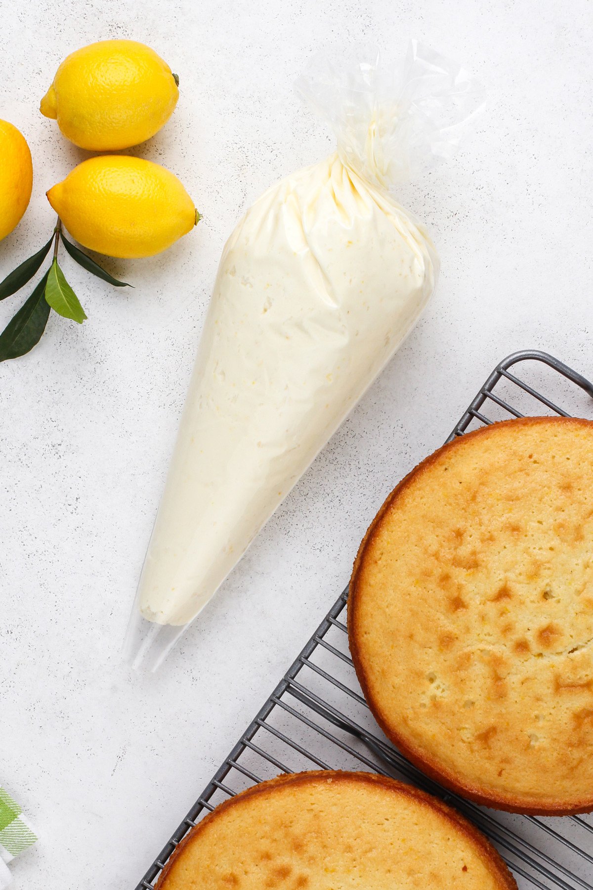 Piping bag filled with lemon buttercream frosting next to cake layers on a wire rack.